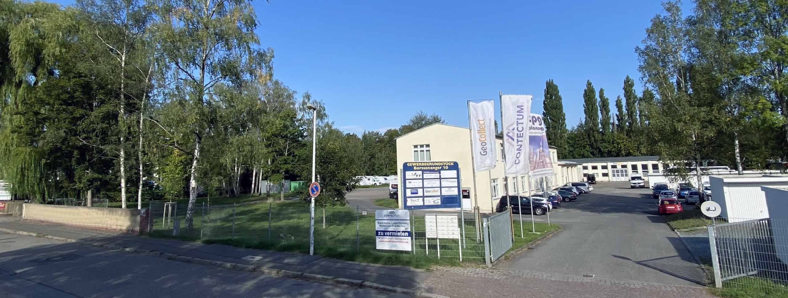 Gewerbestandort Borssenanger 10 mit Firmenlogos, Fahnen und Parkplatz.